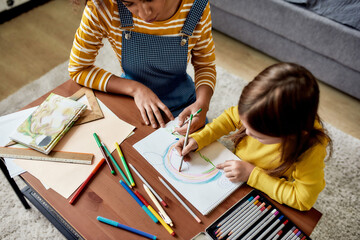 Education and Care. Caucasian little girl spending time with african american baby sitter. They are drawing a mouse together