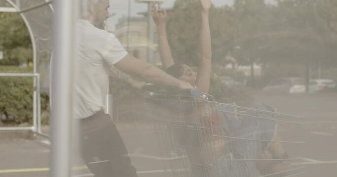 Couple playing with shopping trolley in car park and having fun together