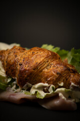 Salty breakfast with a croissant and ham and salad in a black background. Italian snack. 