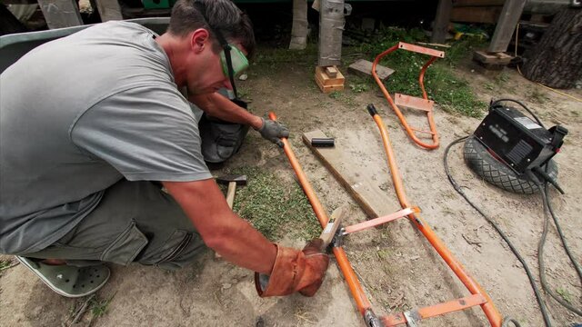 Timelapse of a man in a welding mask and welders leathers is welding broken wheel barrow