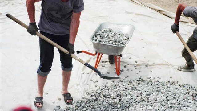 Timelapse view from above of two workers putting gravel into the wheel barrow for transportation it