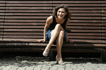Fototapeta na wymiar Brunette girl sits on a park bench and her hair flutters in the wind
