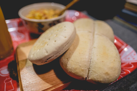 Red plastic tray with wood table with bread (hallulla and marraqueta), a bowl with scrambled eggs with tomato and a glass with fruit juice