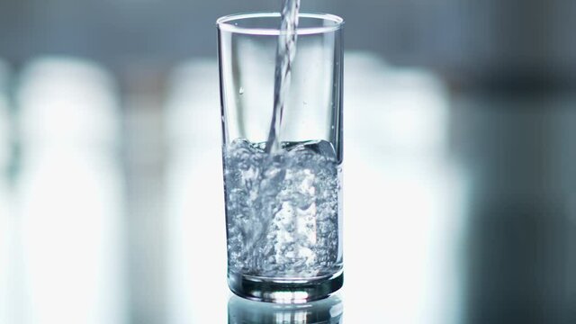 Pure water is poured into a glass beaker on a light background, close-up