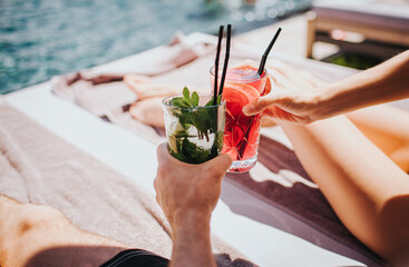 Young hot couple resting at swimpool. Picture of man's and woman's hands holding cocktails. Cool drink with ice inside glass. Enjoy summer vacation at swimming pool. Resort spa place.