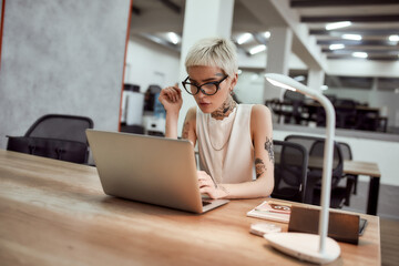 Inspiration. Stylish and beautiful tattooed business lady in eyewear working with laptop while...