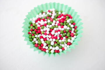 Green, pink and white round sprinkles in a teal green cupcake case container.  Macro shot with top down view focusing on the cake decorations.  White background with space for copy text