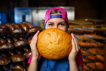 The stage of baking in a bakery. Portrait of a baker girl with bread in her hands against the background of shelving in a bakery. Hands of a baker with bread. Industrial bread production