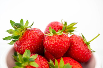 Close up macro image of vivid red strawberries with green stalks against a white background.  Complementary colour scheme with white negative space above food for copy text or customisation