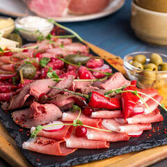 Fototapeta premium Appetizer with salami, ham, roast beef, prosciutto and sausages on a wooden board. Closeup