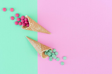 Two ice cream cones off set to left side of frame with candy sweets spilling out.  Complementary colours of green and pink.Food photo in flat lay style against vivid background with copy space