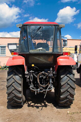 Obraz premium Red tractor from the backside with big tractor tires. A close up shot of a brand new tractor's tire on a sunny day in germany Sauerland.