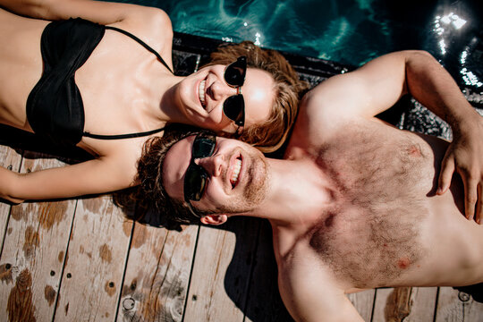 Young hot couple resting together. Picture of cheerful man and woman lying close to each other and enjoying company. Looking up and smile. Resort spa time during summer vacation.