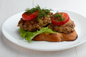 sandwich with cutlet, lettuce and tomato slices on a white plate on a white wooden background