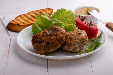 meatballs with vegetables on a white plate with a slice of toasted bread and mustard on a white wooden background