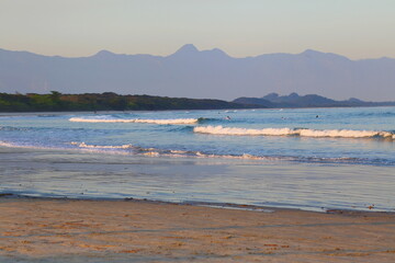 Blue ocean with calm waves. In the background vegetation and far away mountains.  Itaguare beach, Bertioga, Brazil 