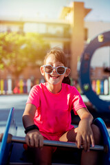 girl smiling with sunglasses, playing seesaw in city park, lifestyle concept