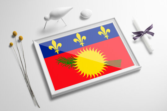 Guadeloupe flag in wooden frame on table. White natural soft concept, national celebration theme.