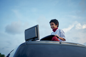 Boy in school uniform playing internet games on top of car roof, New Normal Education concept