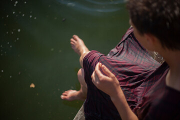 A girl in wet clothes is sitting by the lake.