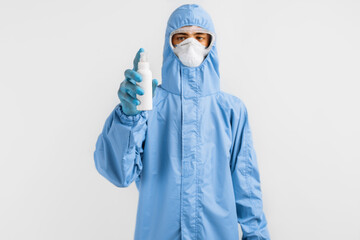 Fototapeta na wymiar male doctor in a protective suit against coronavirus, wearing gloves, glasses and a medical mask, holding a jar of antiseptic, on an white background. Quarantine, coronavirus