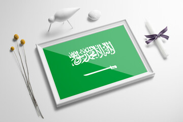 Saudi Arabia flag in wooden frame on table. White natural soft concept, national celebration theme.