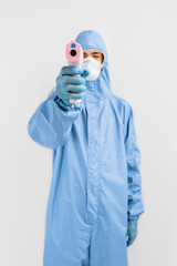 male doctor in a protective suit from the coronavirus, a medical mask glasses and gloves, uses an infrared non-contact thermometer gun to check body temperature for symptoms of the covid-19 virus