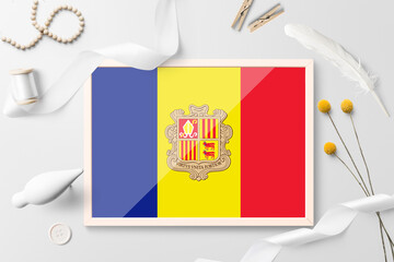 Andorra flag in wooden frame on white creative background. White theme, feather, daisy, button, ribbon objects.
