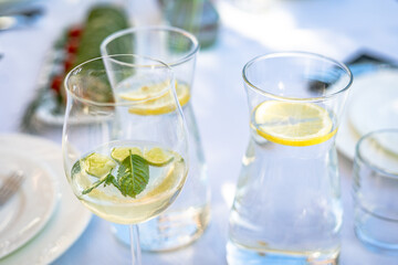 close up of fresh and light alcoholic summer drink with Prosecco yellow lemon and green mint leaf on beautiful bright party table