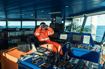 Filipino deck Officer on bridge of vessel or ship wearing coverall. He is looking through binoculars. COLREG navigaton watch at sea