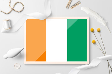 Cote D'Ivoire flag in wooden frame on white creative background. White theme, feather, daisy,...