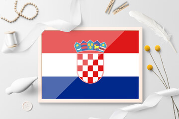 Naklejka premium Croatia flag in wooden frame on white creative background. White theme, feather, daisy, button, ribbon objects.