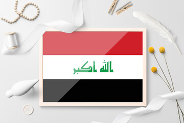 Iraq flag in wooden frame on white creative background. White theme, feather, daisy, button, ribbon objects.