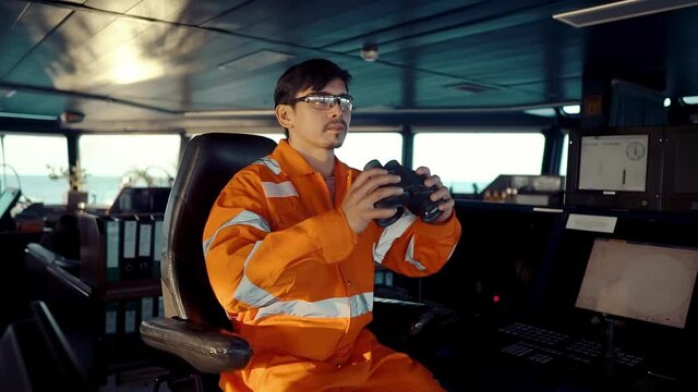 Filipino deck Officer on bridge of vessel or ship wearing coverall. He is looking through binoculars. COLREG navigaton watch at sea