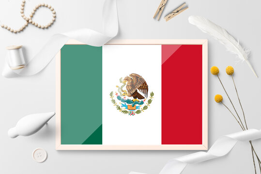 Mexico flag in wooden frame on white creative background. White theme, feather, daisy, button, ribbon objects.
