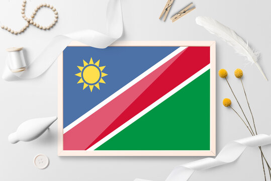 Namibia flag in wooden frame on white creative background. White theme, feather, daisy, button, ribbon objects.