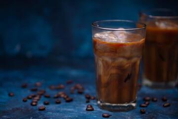 Cold summer drink, iced coffee with cream or milk.Cool drink with coffee grains on blue background