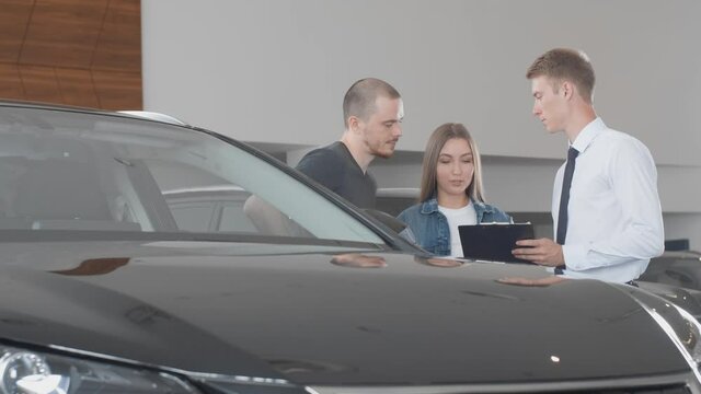 Car dealership Manager shows a luxury car to a couple at a dealership. Concept professionalism agreement contract leasing renting retail car sales