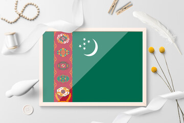 Turkmenistan flag in wooden frame on white creative background. White theme, feather, daisy, button, ribbon objects.