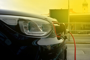 Obraz premium Modern electric car plugged in charging on the street station. New energy vehicles, environment friendly alternative energy for cars