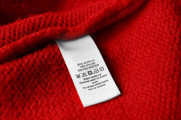 Clothing label with care symbols and material content on red sweater, closeup view