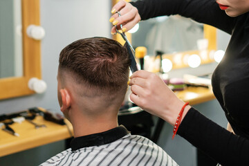 Hairdresser performs a men's haircut. Attractive female cuts a man in the salon.