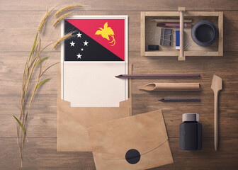 Papua New Guinea invitation, celebration letter concept. Flag with craft paper and envelope. Retro theme with divide, ink, wooden pen objects.