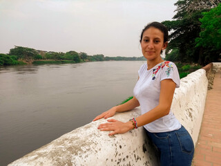 Linda chica sonriendo apoyada en el muro a la orilla del río