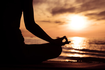 Silhouette of hand woman practicing yoga on the beach at sunset or sunrise. women do yoga. women exercising yoga in the beach.Young girl meditating in lotus posture.