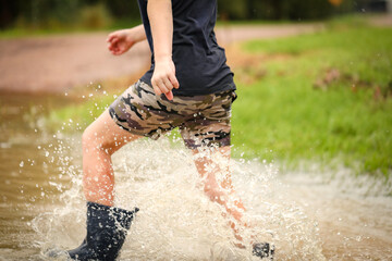 Boy walking through flooded creek wearing gumboots getting very wet, no face visible