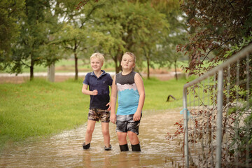 Fototapeta na wymiar Boys playing in flooded creek with wet gumboots