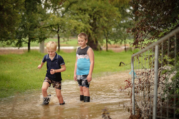 Fototapeta premium Two young brothers walking along flooded creek wearing gumboots in water