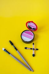 Lip gloss and cosmetic brushes on a yellow background
