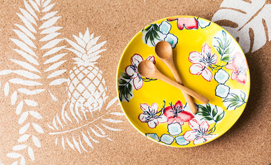 Plano cenital de llamativo y colorido plato junto a dos cucharas hechas de madera y sobre una plancha de corcho pintada con stencil  bajo iluminación natural